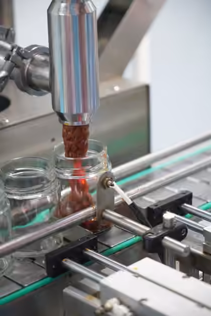 A filling head dispensing sauce into a glass jar